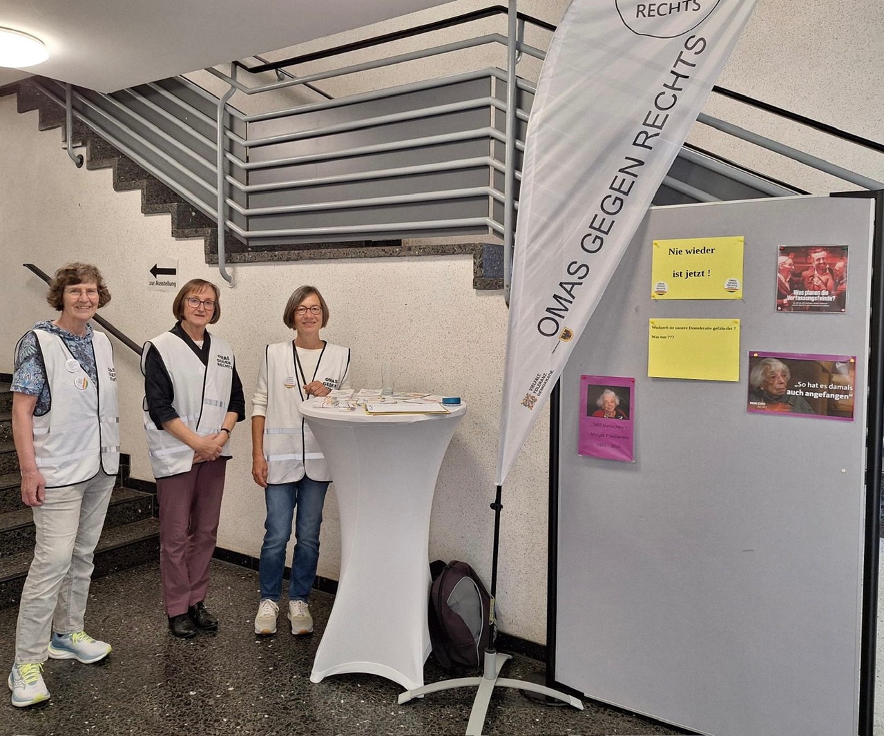 Informationsstand der Omas gegen Rechts mit Roll-up-Banner und Infomaterial, zwei Personen am Tisch.